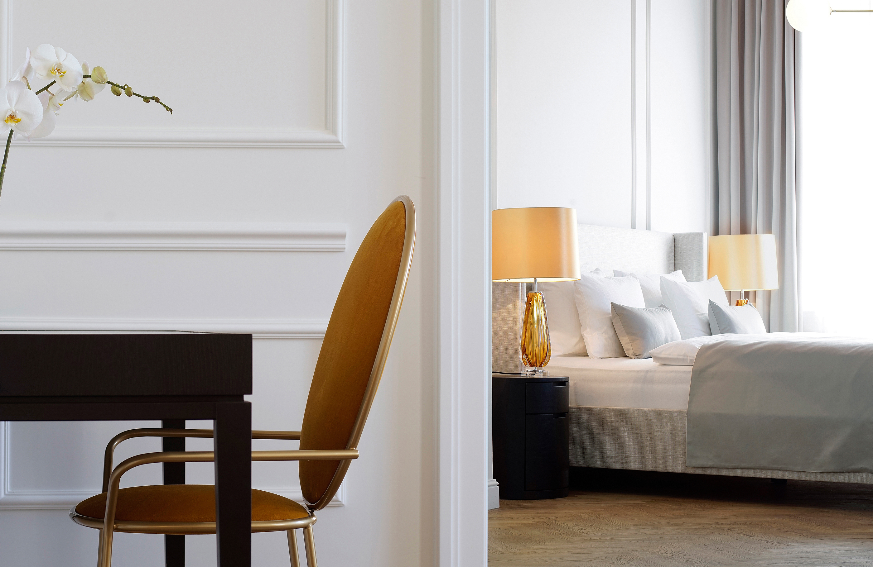 Seitliche Detailaufnahme eines orange, goldenen Stuhls mit dem angrenzenden Schlafzimmer im Hintergrund