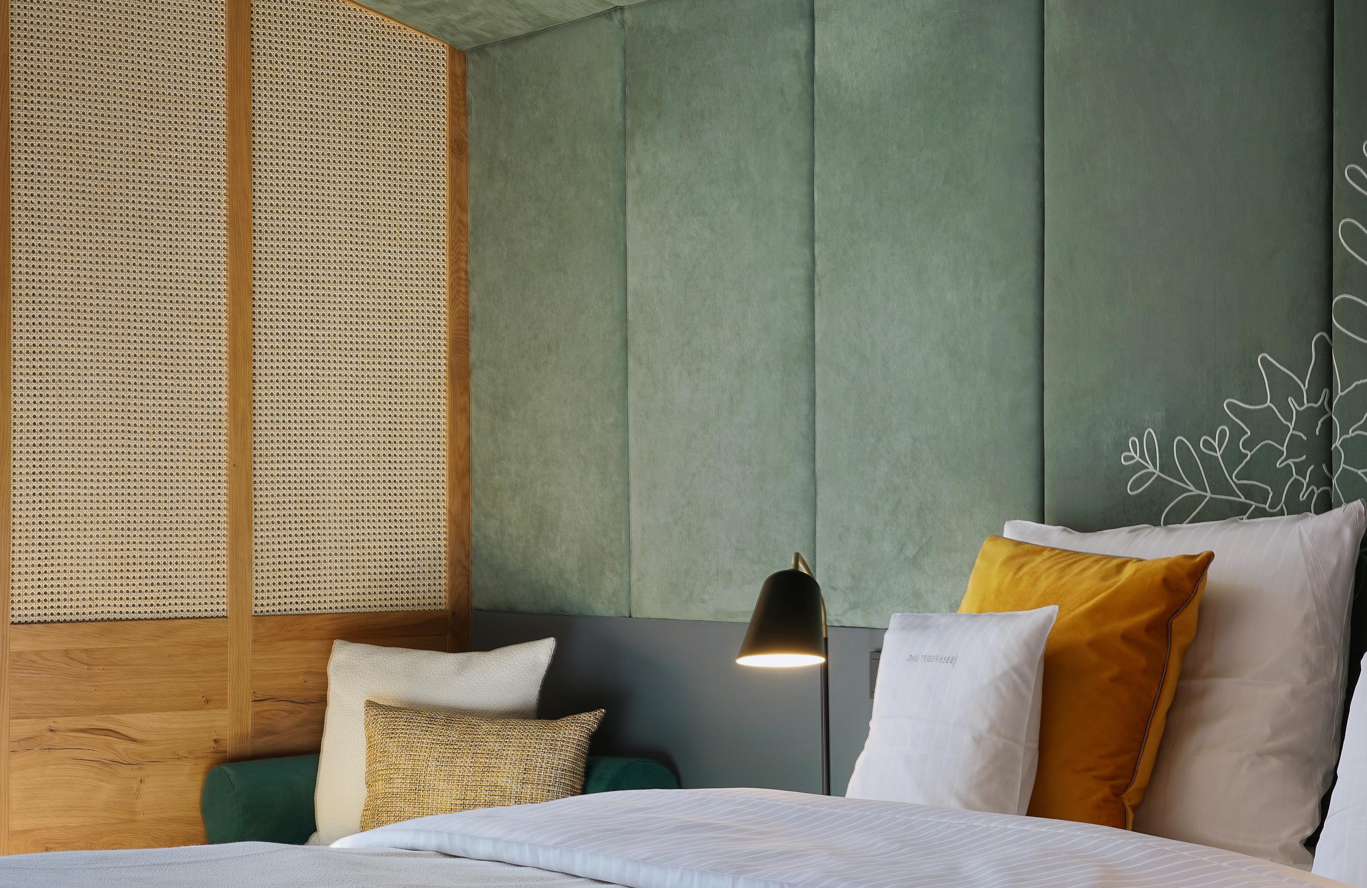 Detailaufnahme des Kopfendes vom Bett vor einer Wand mit salbeigrüner Polsterung