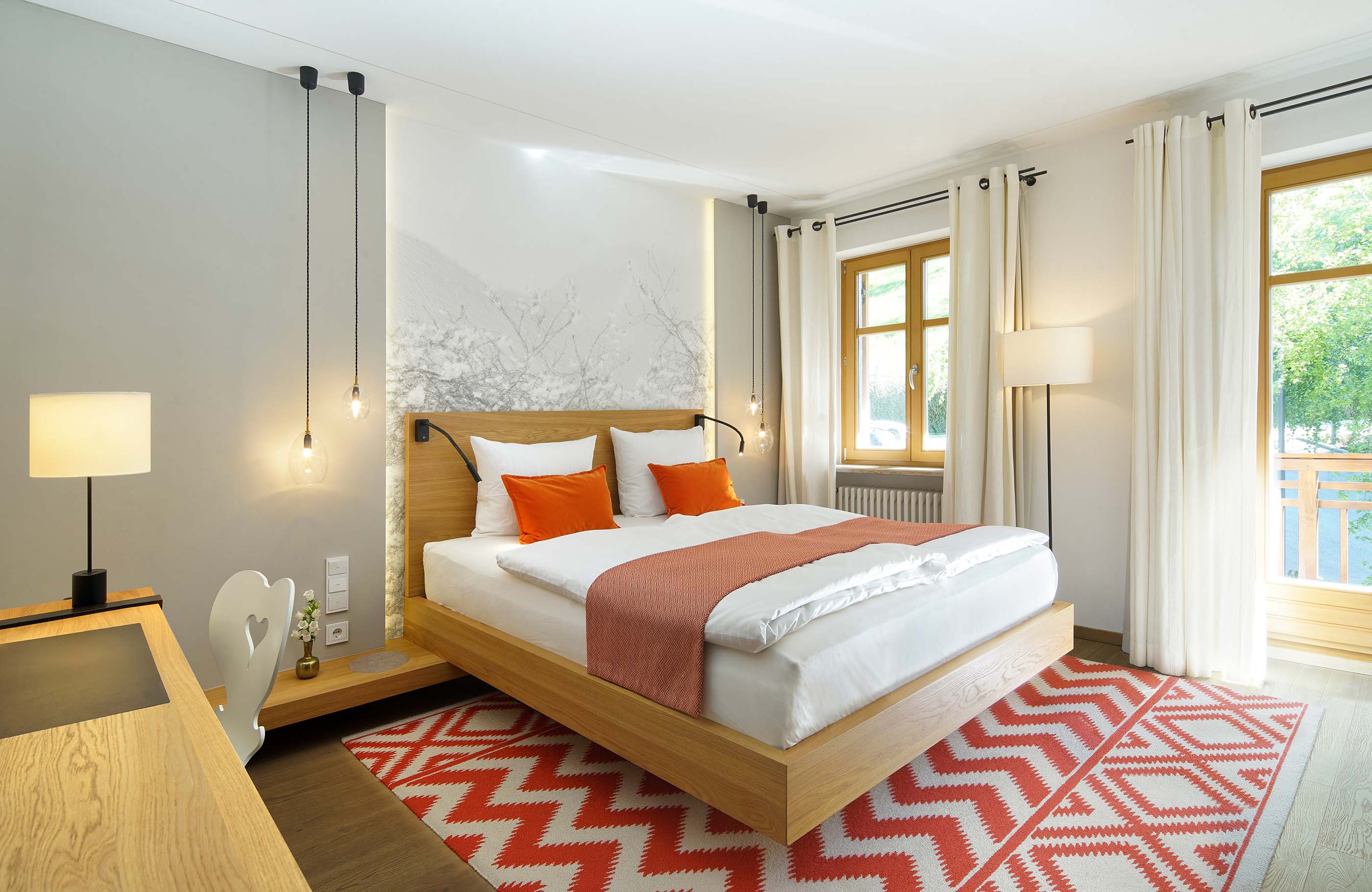 Aufnahme in einem hellen Schlafzimmer mit rotem gemustertem Teppich, Schreibtisch und hellen Fenstern