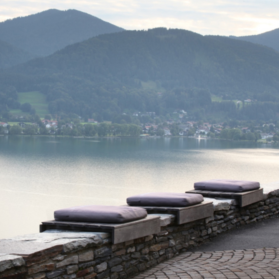 Drei Sitzkissen liegen auf einer Mauer am Tegernsee
