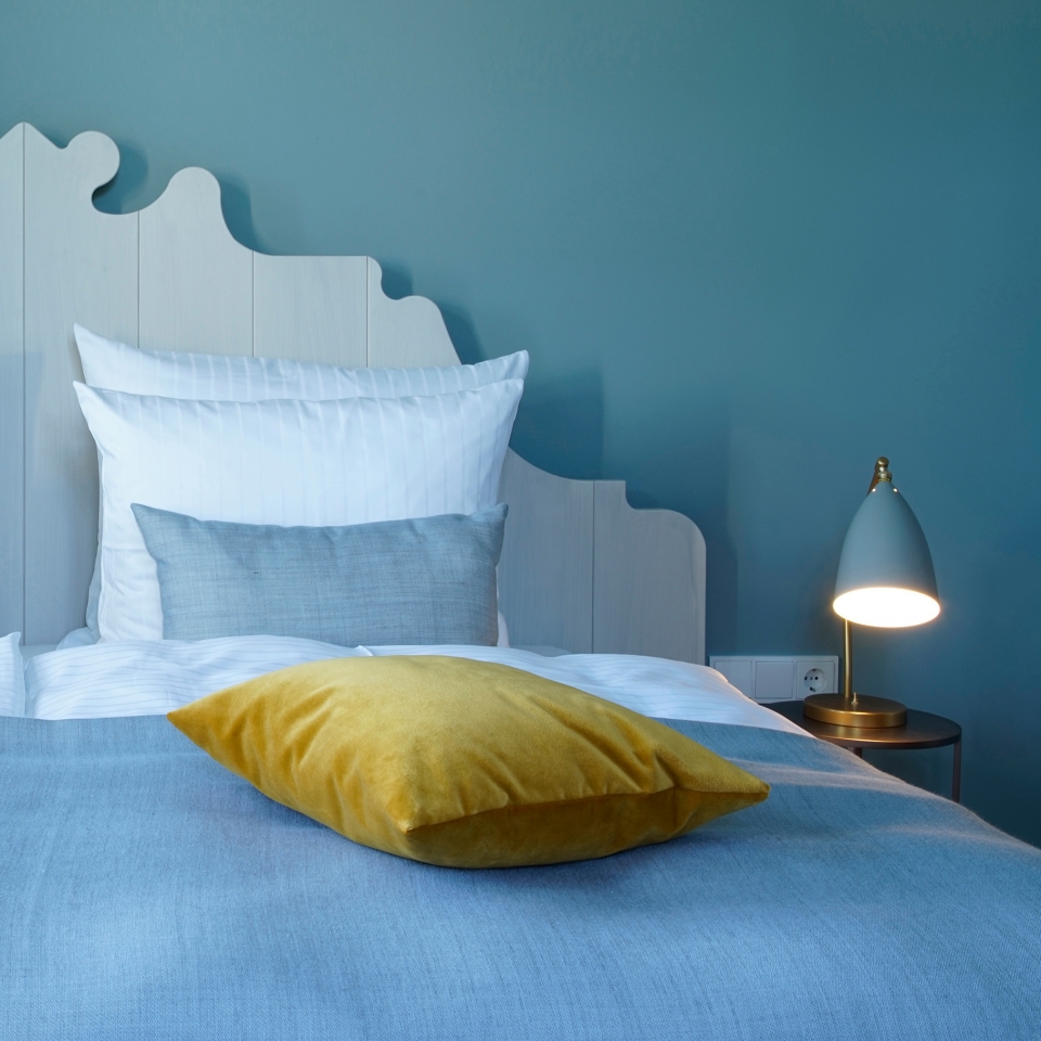 Ein gelbes Kissen liegt auf einem gemütlichem Bett mit hellblauer Tagesdecke