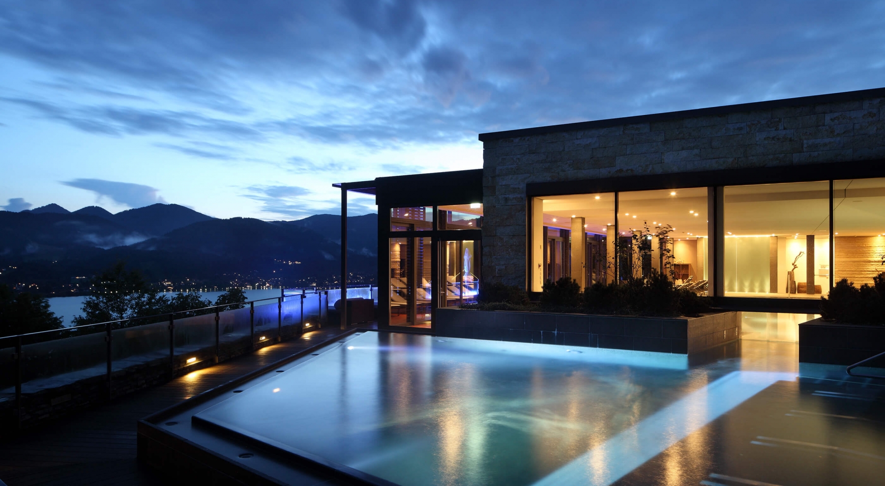 Die Außenansicht des Hotels und der Außenpool bei Nacht mit Blick auf den Tegernsee